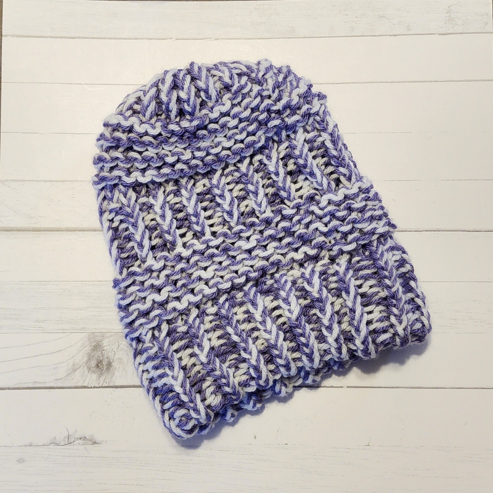 A purple and white crochet beanie hat on a white-wash boarded table.